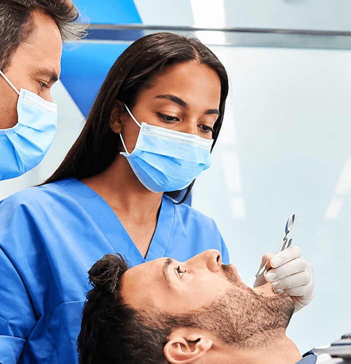 Two dentists in blue scrubs and face masks examining a patient in the treatment room at Apex Dental Hospital, Jaipur